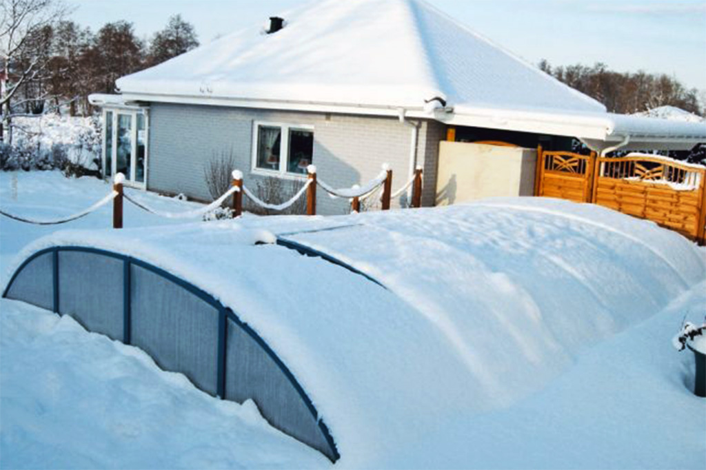 Flache Poolüberdachung Aluna Atlanta unter einer Schneedecke im Winter, mit Haus im Hintergrund