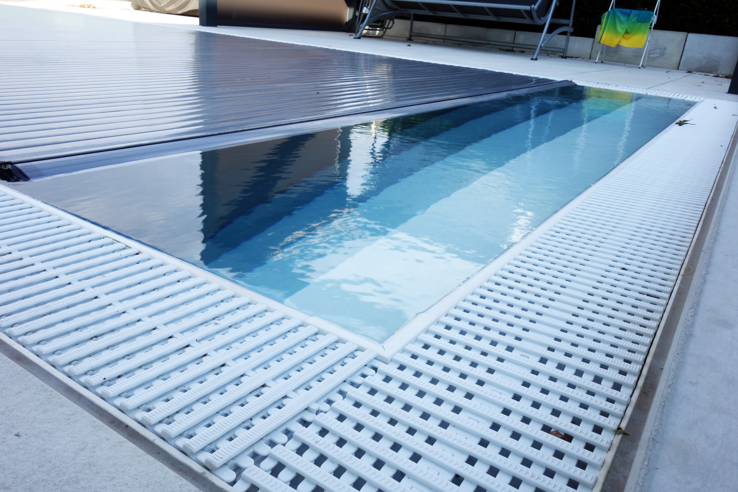 Detailansicht des Überlaufpools mit Unterflurrollladen und den weißen Gitterrosten am Beckenrand.