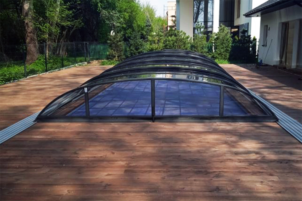 Flache Poolüberdachung Aluna Atlanta mit dunklem Rahmen auf Holzterrasse, seitliche Führungsschienen