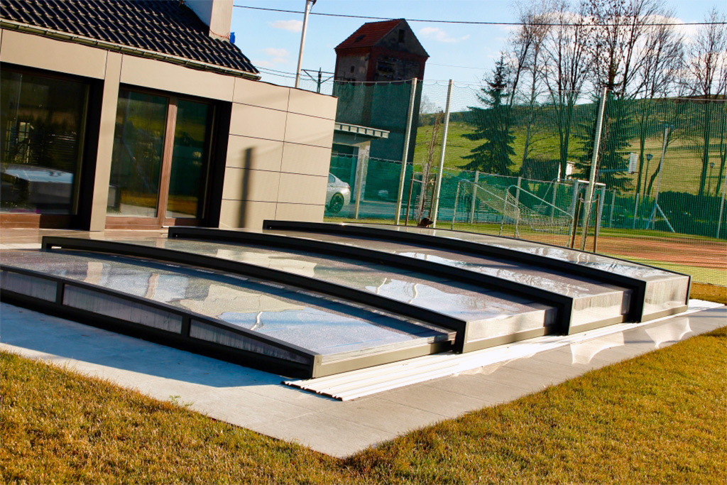 Flache Poolüberdachung Aluna® Exclusive Line R1 mit dunklem Rahmen vor einem modernen Haus