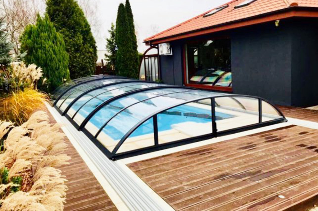 Flache Poolüberdachung Aluna Atlanta mit schwarzem Rahmen auf Holzterrasse, umgeben von Ziergräsern