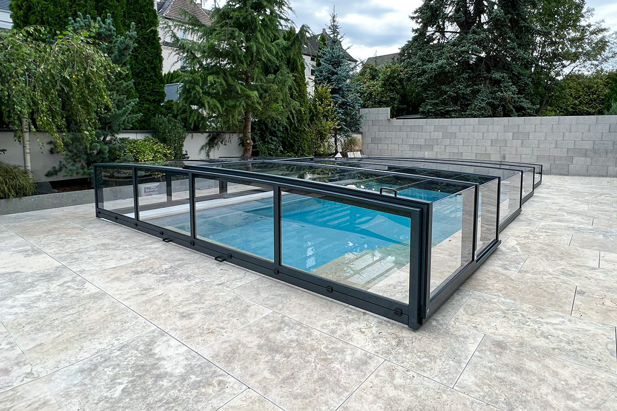 Flache Poolüberdachung Aluna® Exclusive Line R1 mit transparenten Seitenwänden und anthrazitfarbenen Profilen.
