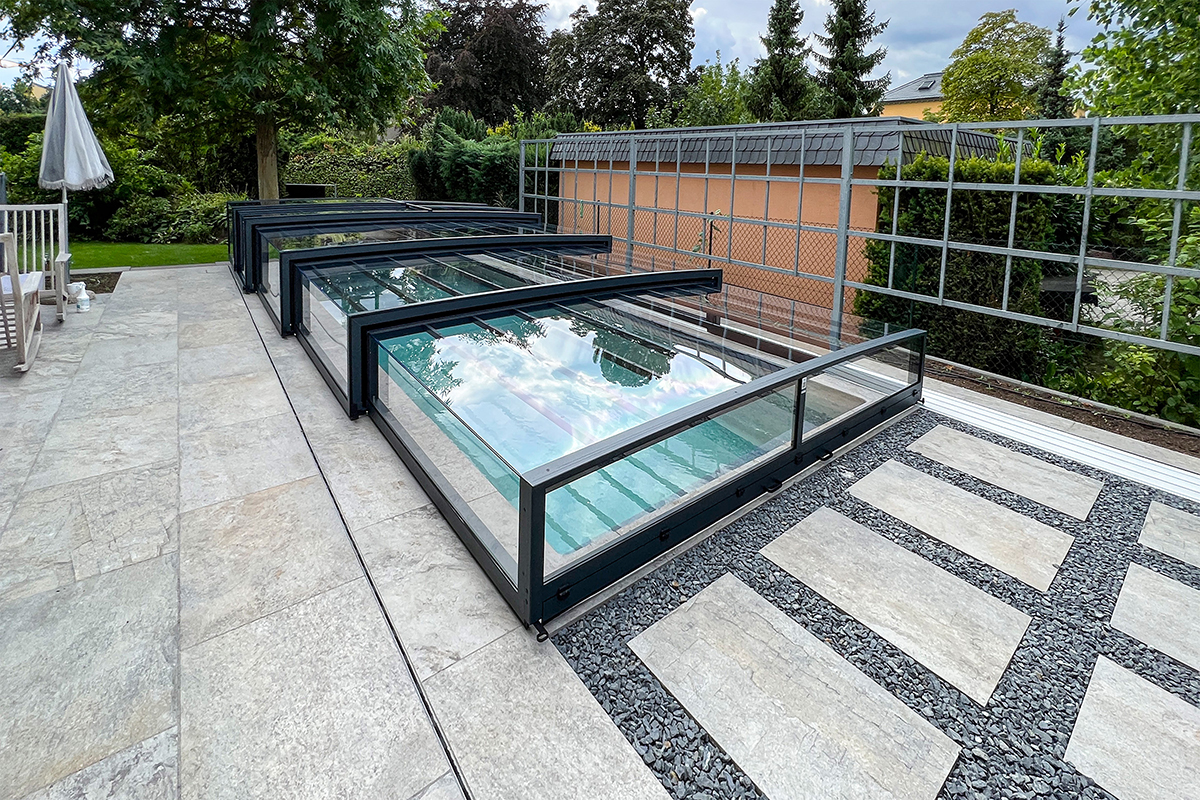 Flache Poolüberdachung Aluna Exclusive Line R1 mit dunklem Rahmen und transparenten Elementen auf Terrasse