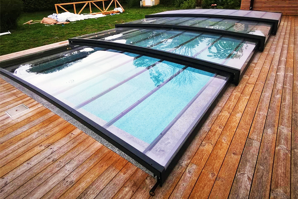 Flache Poolüberdachung Aluna® Exclusive Line R1 mit dunklem Rahmen auf Holzterrasse, Pool mit blauen Fliesen