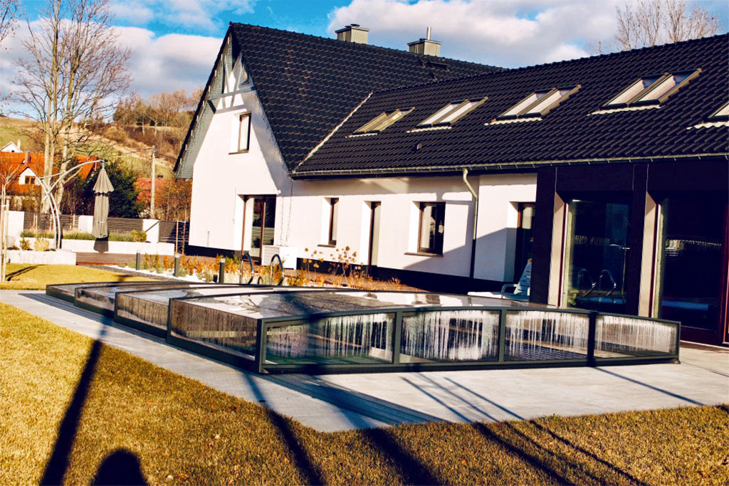 Flache Poolüberdachung Aluna® Exclusive Line R1 vor einem modernen Wohnhaus mit Garten