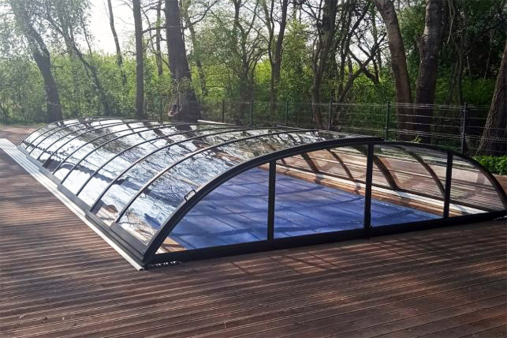 Flache Poolüberdachung Aluna Atlanta mit schwarzem Rahmen auf Holzterrasse, im Hintergrund Bäume