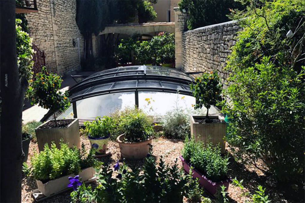Runde Poolüberdachung Aluna Atlanta in einem mediterranen Garten mit Steinmauern und Pflanzen