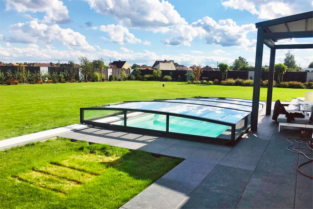 Flache Poolüberdachung Aluna Exclusive Line R1 mit dunklem Rahmen über einem Pool im Garten