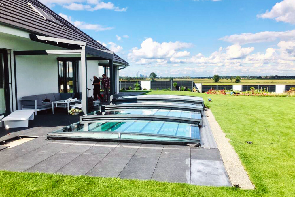 Flache Poolüberdachung Aluna Exclusive Line R1 vor einem modernen Haus mit Terrasse und Rasen.